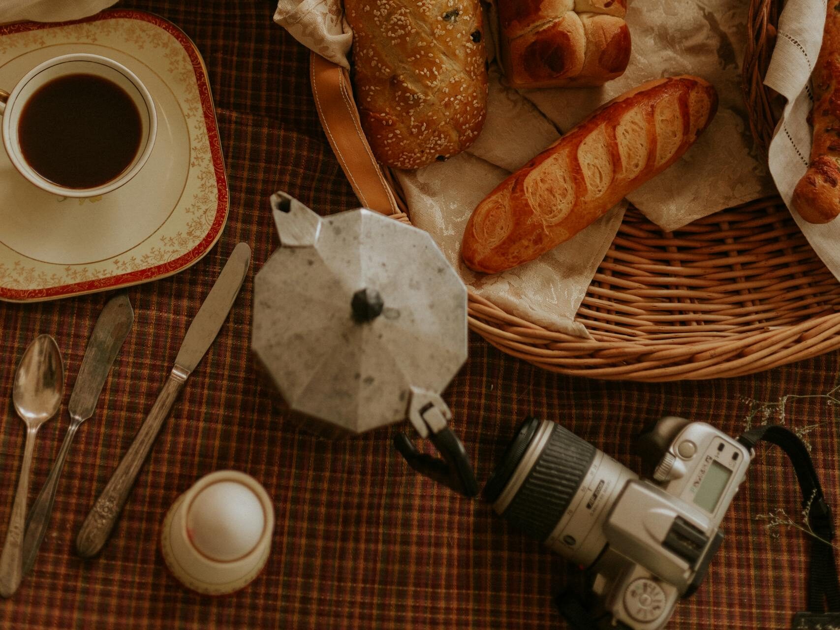 Ciepłe, rustykalne otoczenie w stylu vintage, świeży chleb, filiżanka kawy i aparat na kraciastym obrusie.